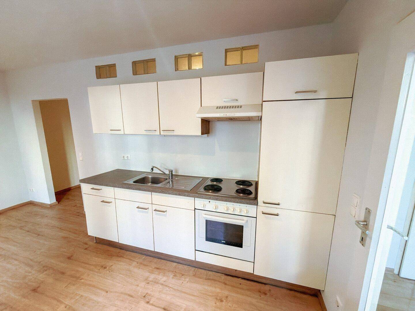Kompakte Einbauküche mit weißen Schränken, Kochfeld und Backofen in einem hellen Raum.
