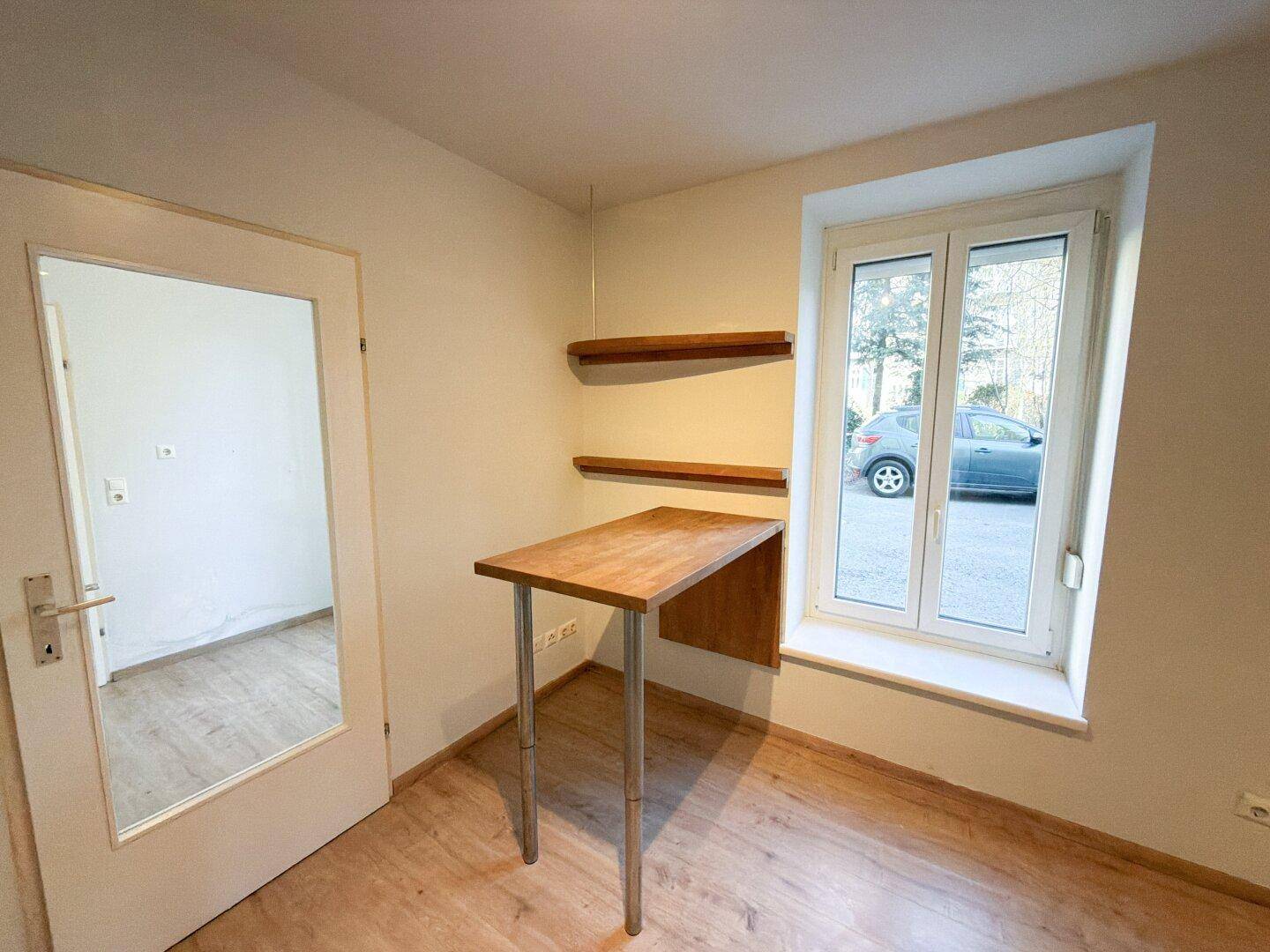 Heller Bereich mit einem kleinen Holztisch und Regalen neben einem Fenster mit Blick nach draußen.