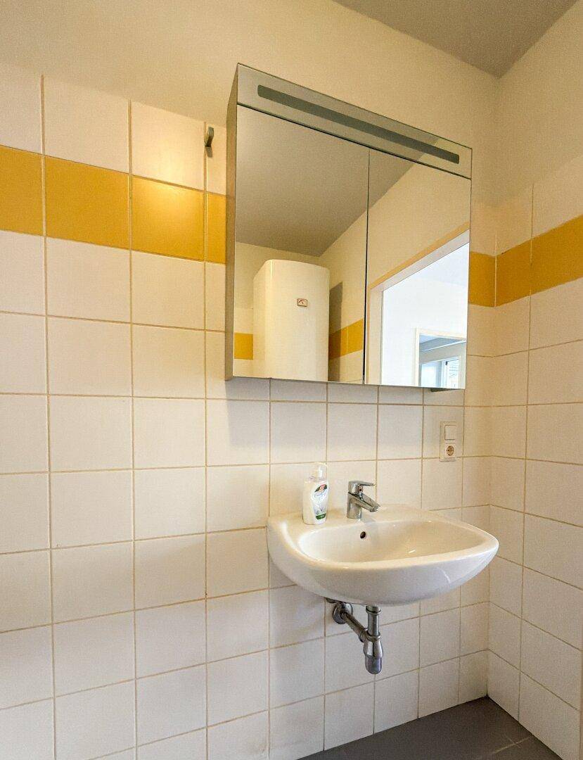 Waschbecken mit Spiegelschrank in einem Badezimmer mit weißen Fliesen und gelbem Streifen.
