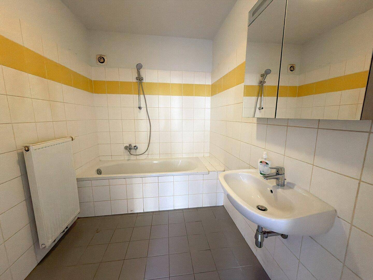 Badezimmer mit Badewanne, Waschbecken und weißen Fliesen mit gelbem Akzentstreifen.