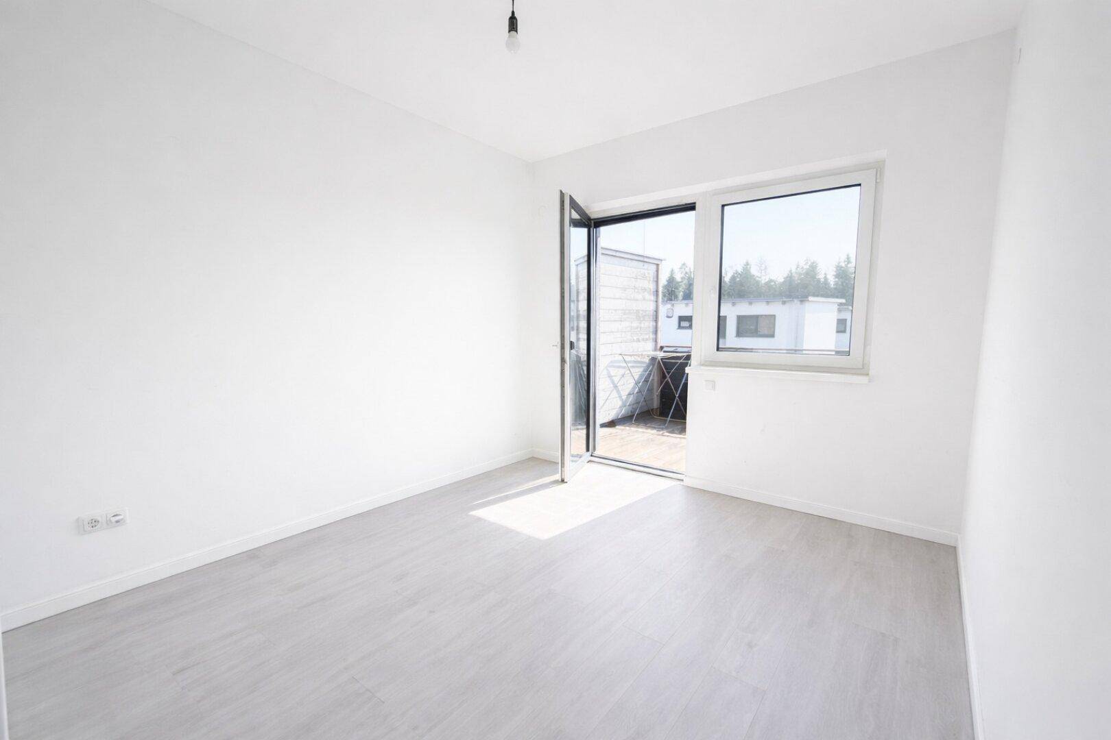Helles Schlafzimmer mit hellem Laminatboden und Zugang zu einem kleinen Balkon.