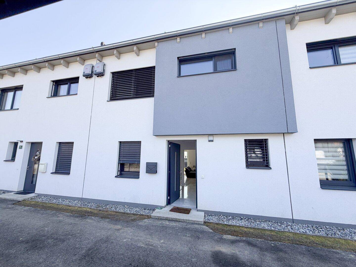Moderne Reihenhausfassade mit weißem Putz und grauen Akzenten, einladender Eingangsbereich.