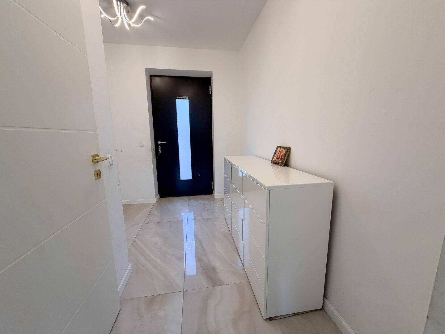 Heller Eingangsbereich mit modernen Fliesen und einer weißen Kommode, führt zur Wohnungstür.