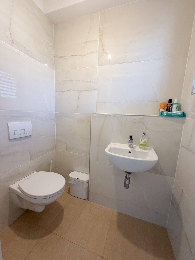 Modernes Gäste-WC mit Wand-WC und kleinem Waschbecken, komplett gefliest und praktisch.