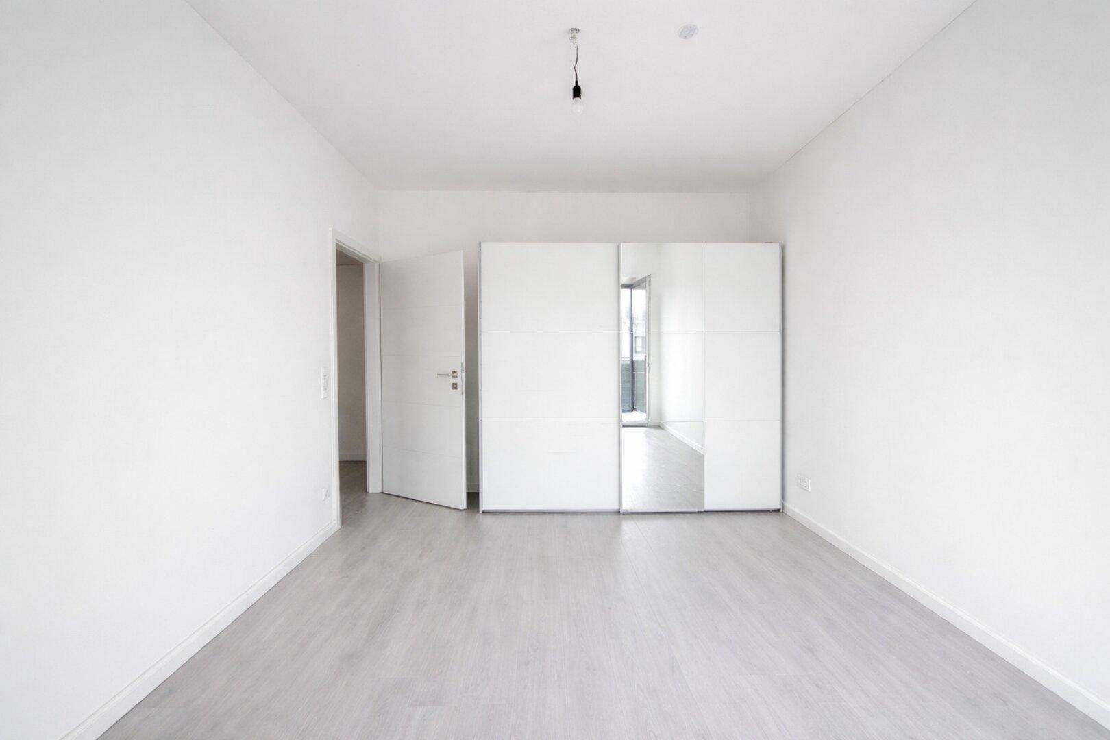 Geräumiges Schlafzimmer mit weißem Schiebetürenschrank und hellem Laminatboden, modern und funktional.