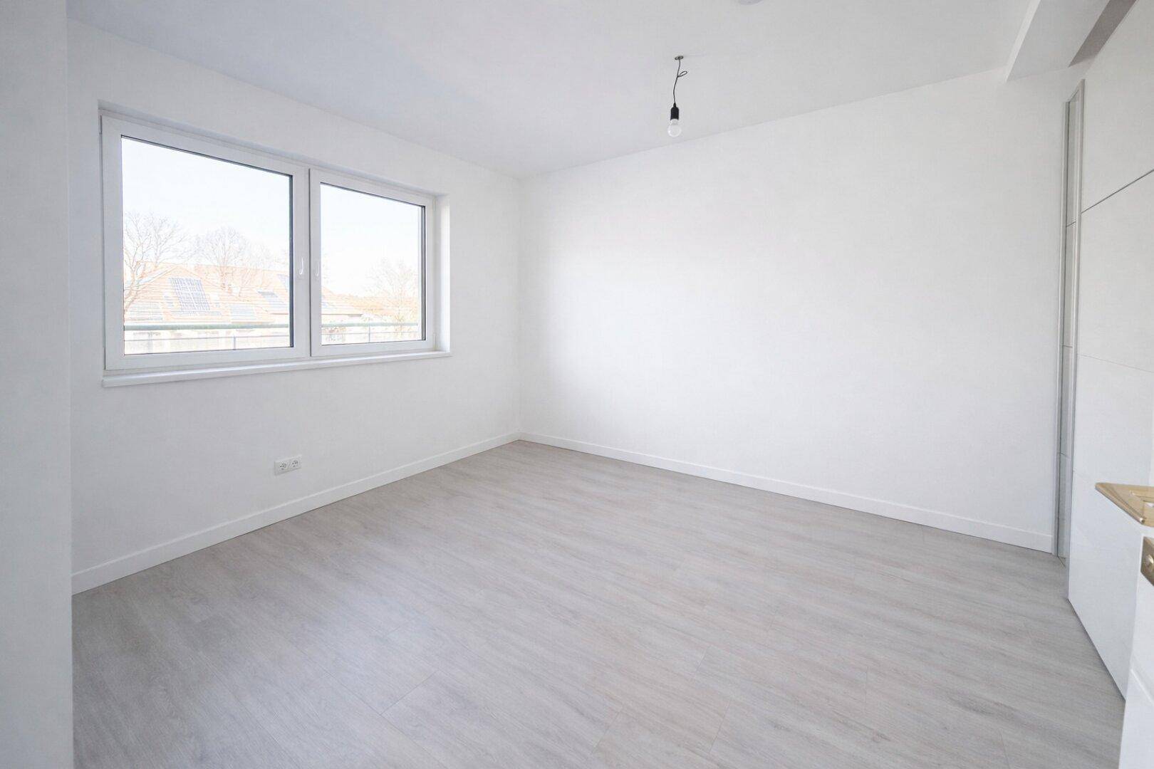 Lichtdurchflutetes Schlafzimmer mit großen Fenstern und hellem Laminatboden, bietet viel Tageslicht.