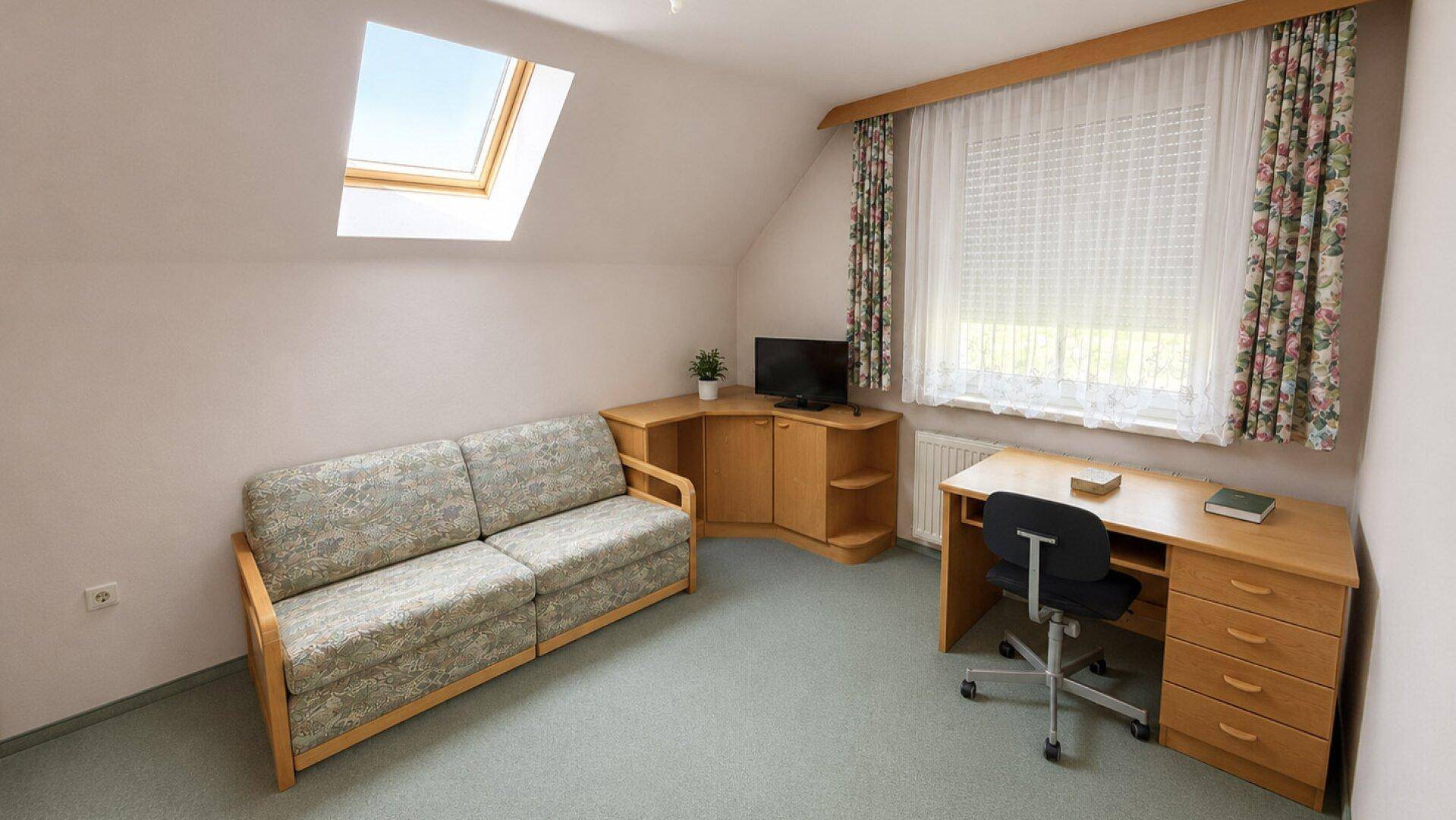 Dachgeschosszimmer mit Sofa, Schreibtisch, Dachfenster und Teppichboden, vielseitig nutzbar.