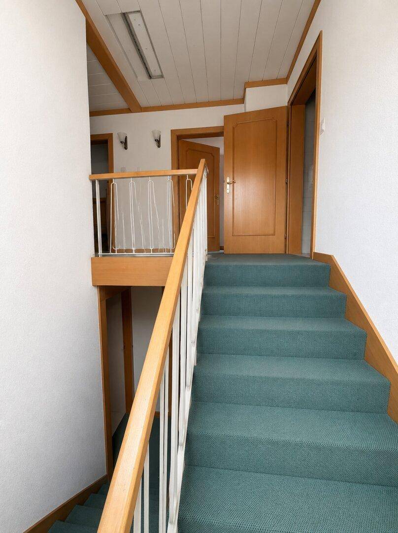 Treppenhaus mit Teppichboden und Holzgeländer, das zu den oberen Etagen führt, hell und sauber.