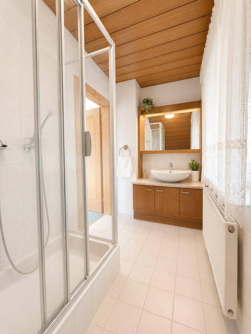 Modernisiertes Badezimmer mit Duschkabine, Waschbecken und Holzdecke, hell und sauber.