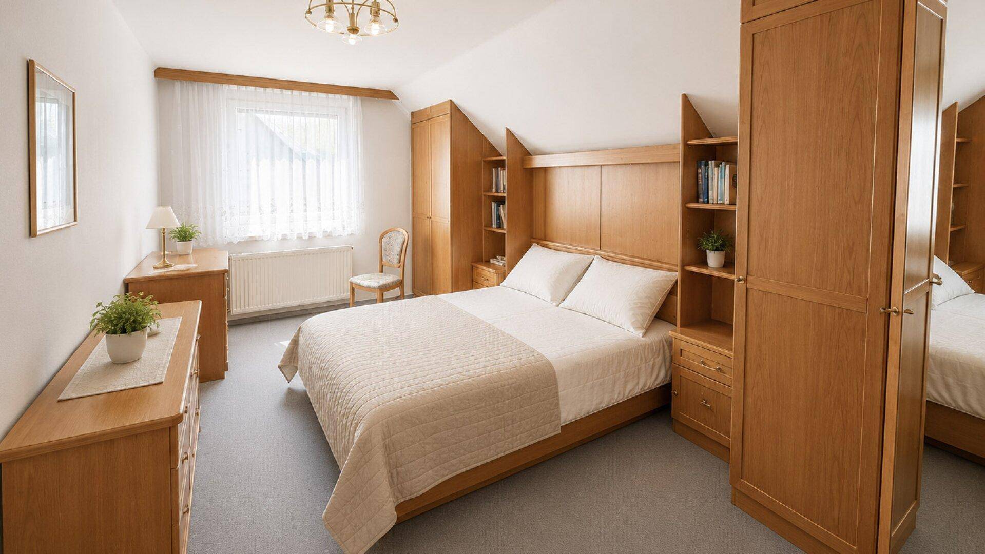 Helles Schlafzimmer im Dachgeschoss mit Doppelbett, Holzmöbeln und Teppichboden, gemütlich eingerichtet.