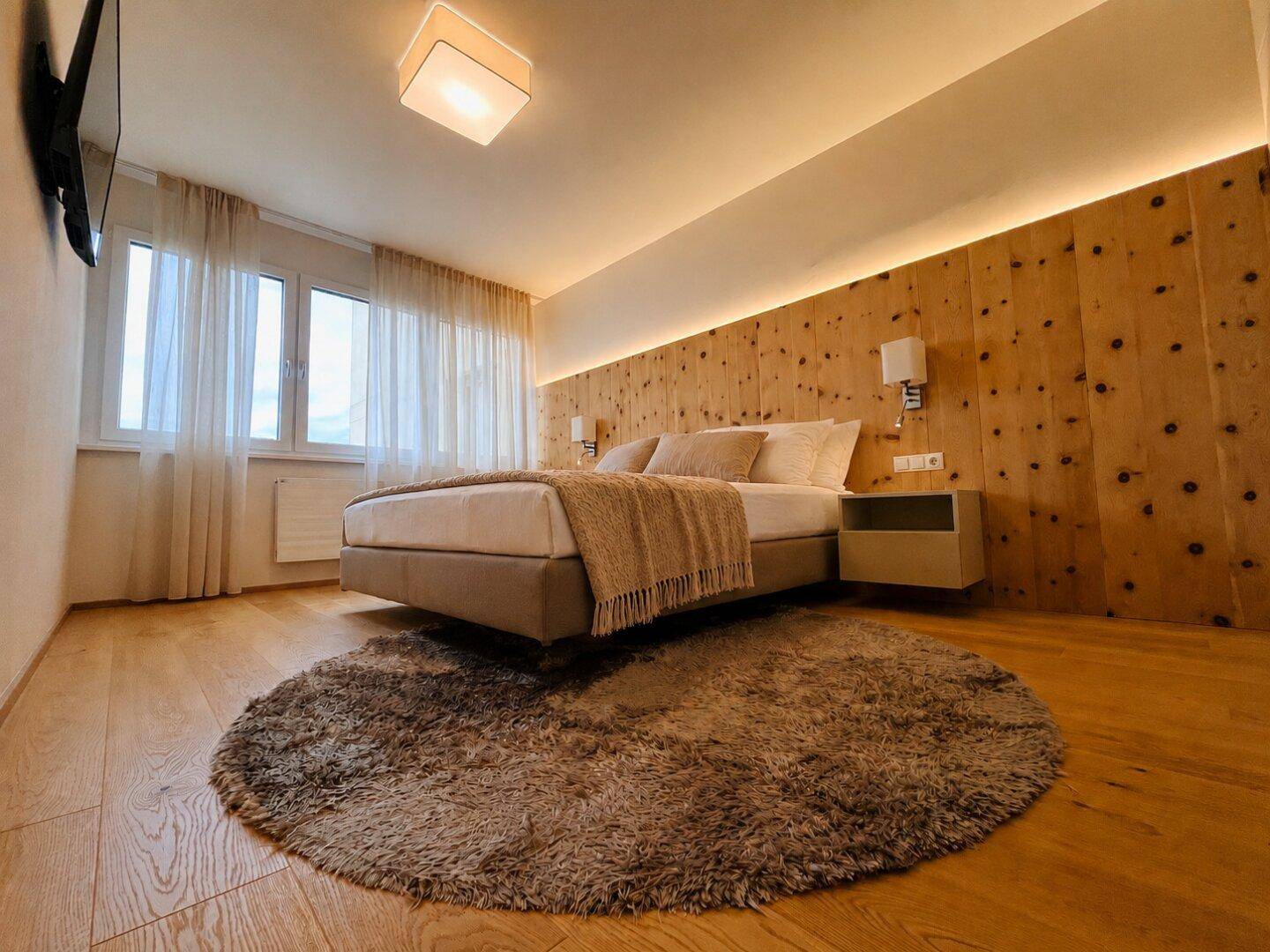 Gemütliches Schlafzimmer mit Holzboden, Holzwandverkleidung und indirekter Beleuchtung.
