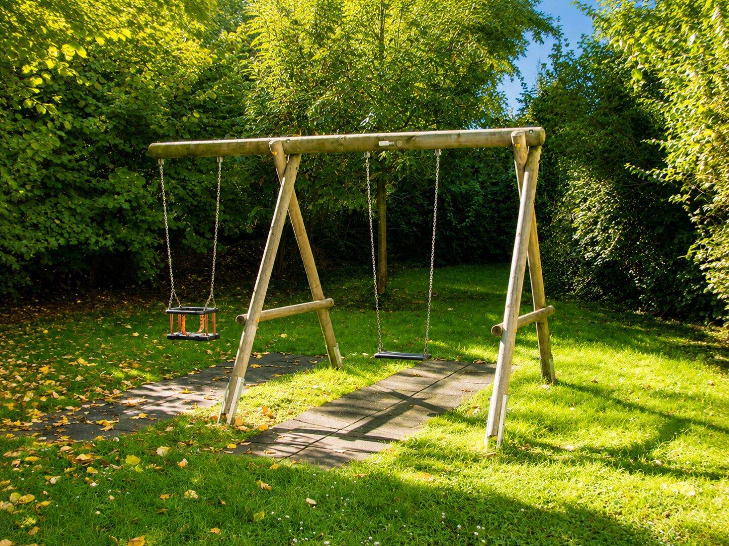 Schaukelbereich auf einem grünen Spielplatz, umgeben von üppiger Vegetation.