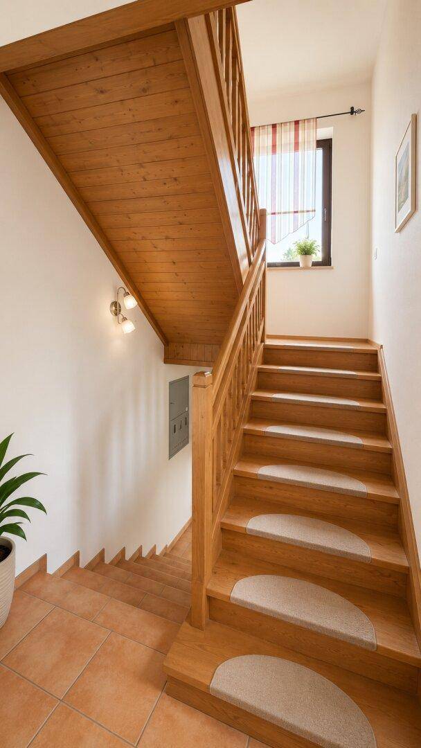 Holztreppe mit Teppichstufen und Fenster, die zu den oberen Etagen führt.