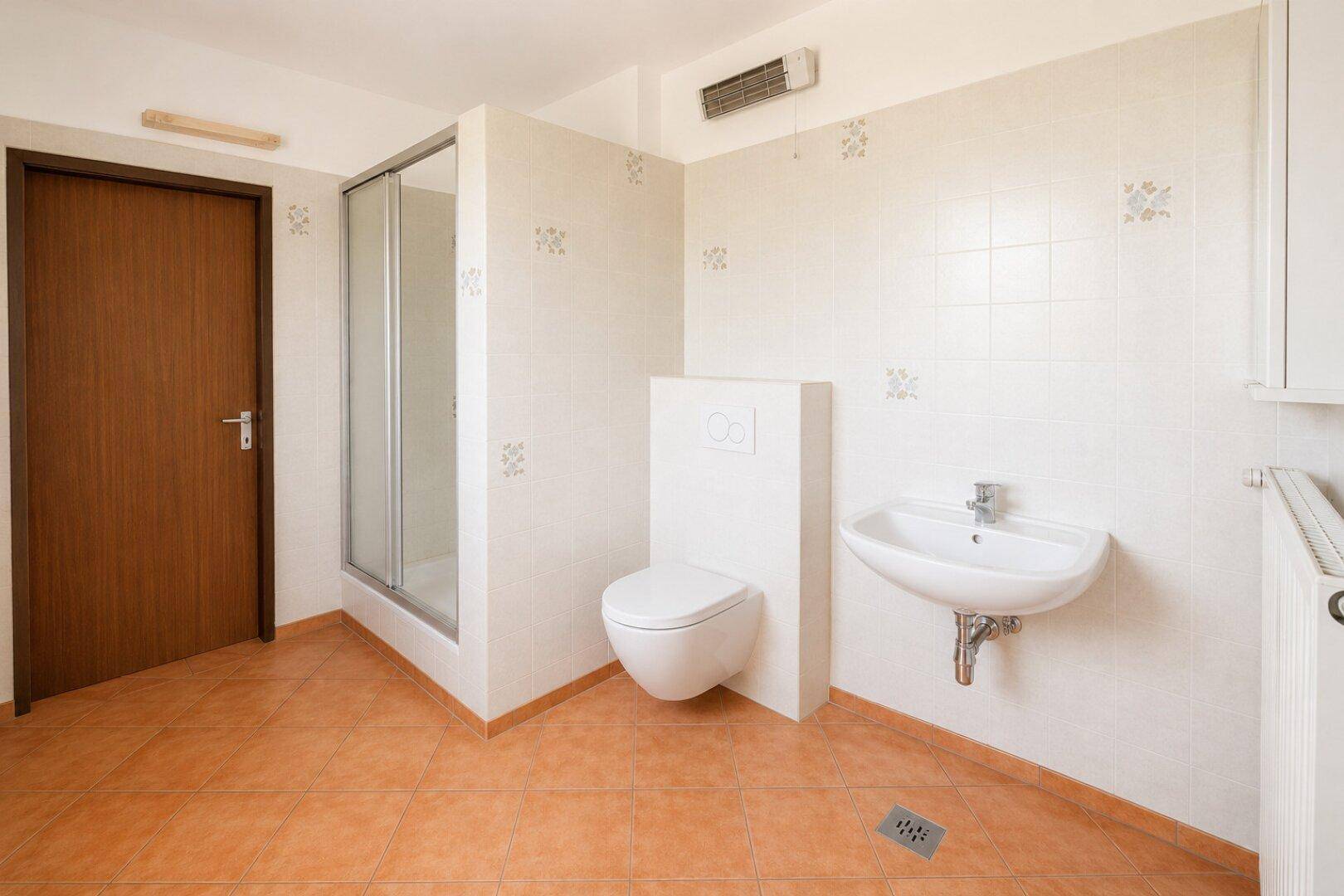 Geräumiges Badezimmer mit Dusche, WC und Waschbecken, gefliestem Boden und Wänden.