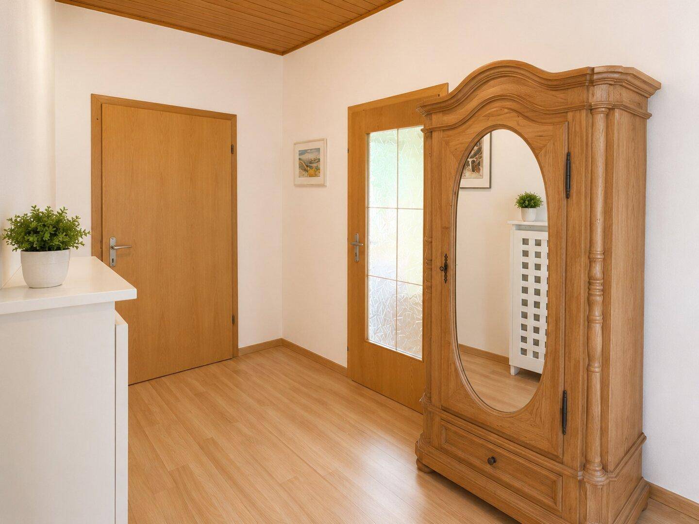 Heller Flur mit Holzboden und einem antiken Holzschrank mit Spiegel.