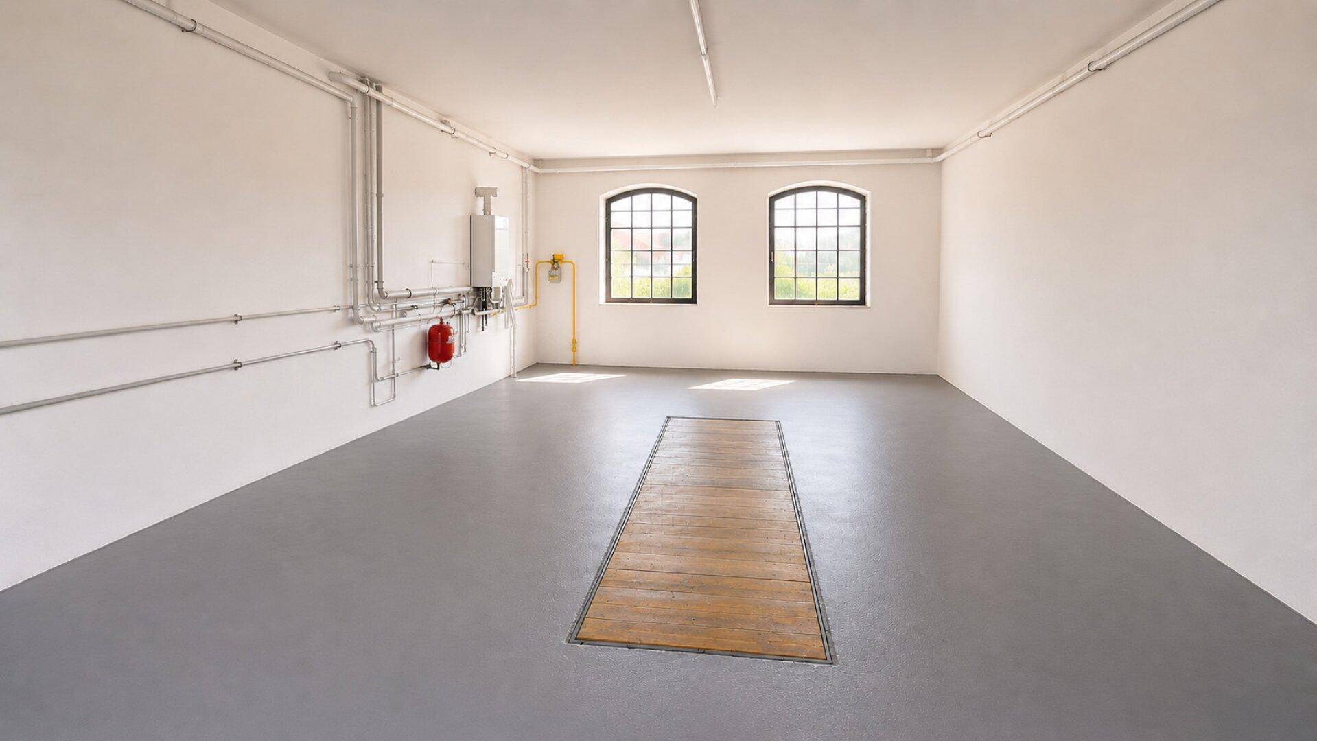 Geräumige Garage oder Werkstatt mit hohen Decken, großen Fenstern und Wartungsgrube.