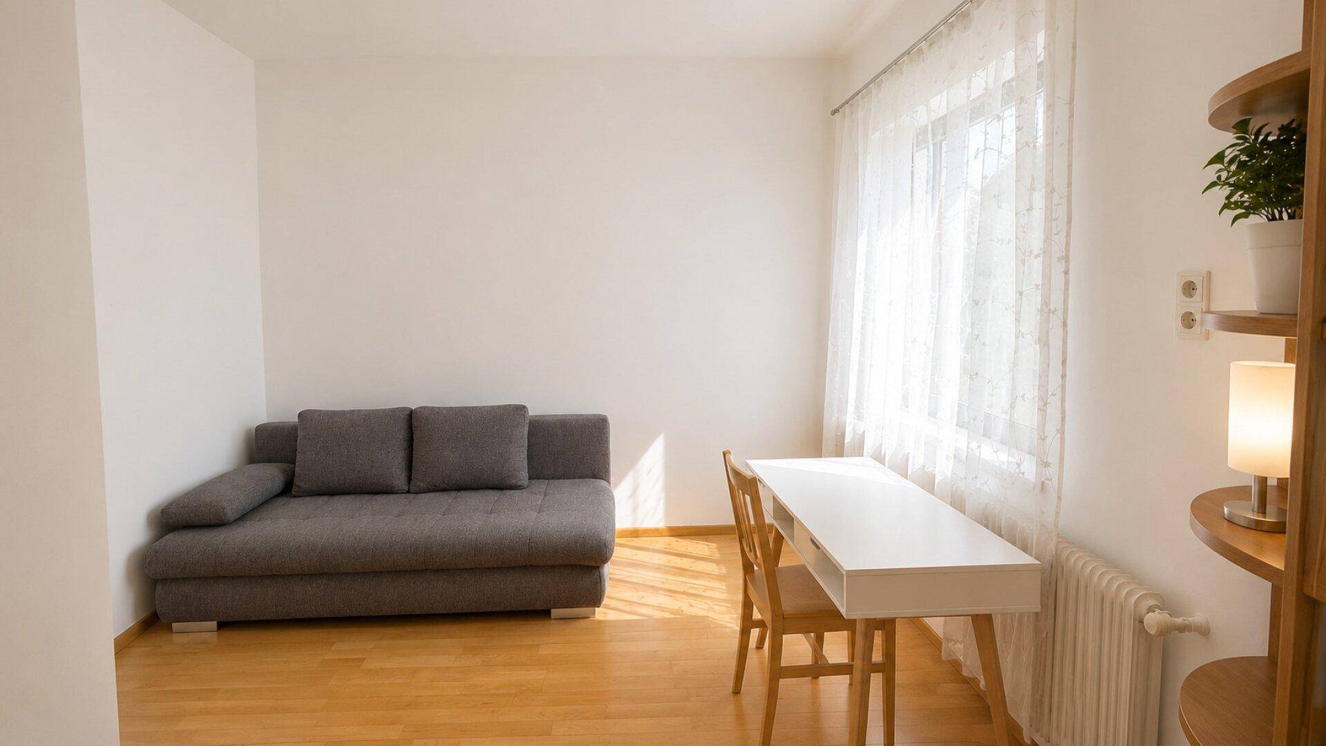 Arbeitsbereich mit Schreibtisch am Fenster, Sofa und hellem Parkettboden.