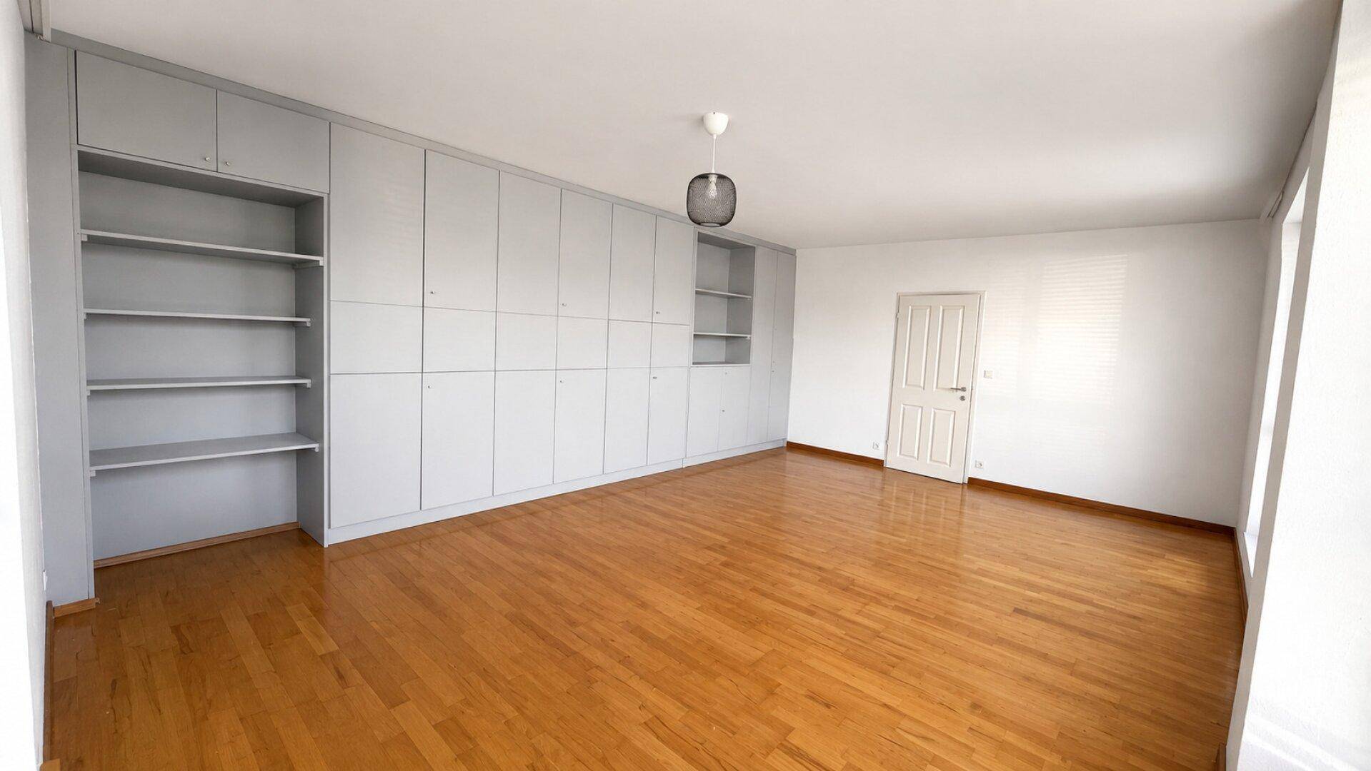 Geräumiges Zimmer mit Holzboden und einer Wand aus grauen Einbauschränken und Regalen.