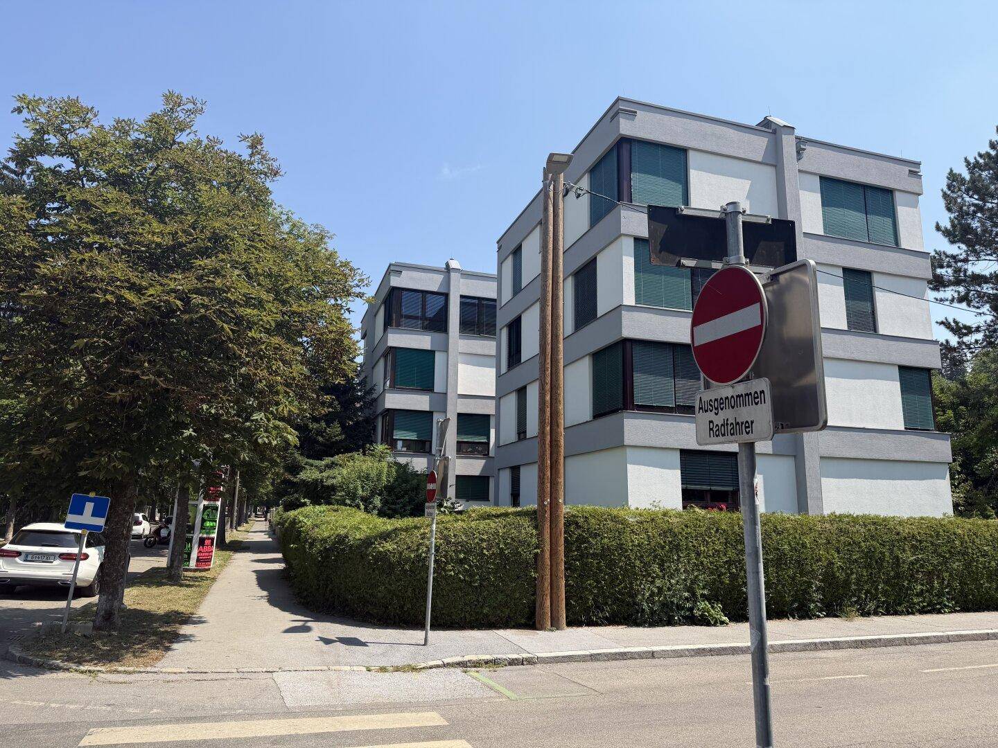 Mehrstöckiges Wohngebäude mit moderner Architektur, umgeben von Bäumen und Hecken.