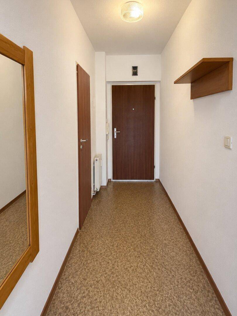 Heller Flur mit Korkboden, weiß gestrichenen Wänden und einem Spiegel.
