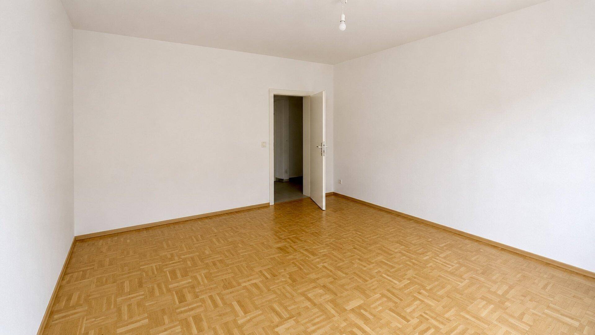 Helles Zimmer mit Parkettboden und weiß gestrichenen Wänden, bereit zur individuellen Gestaltung.