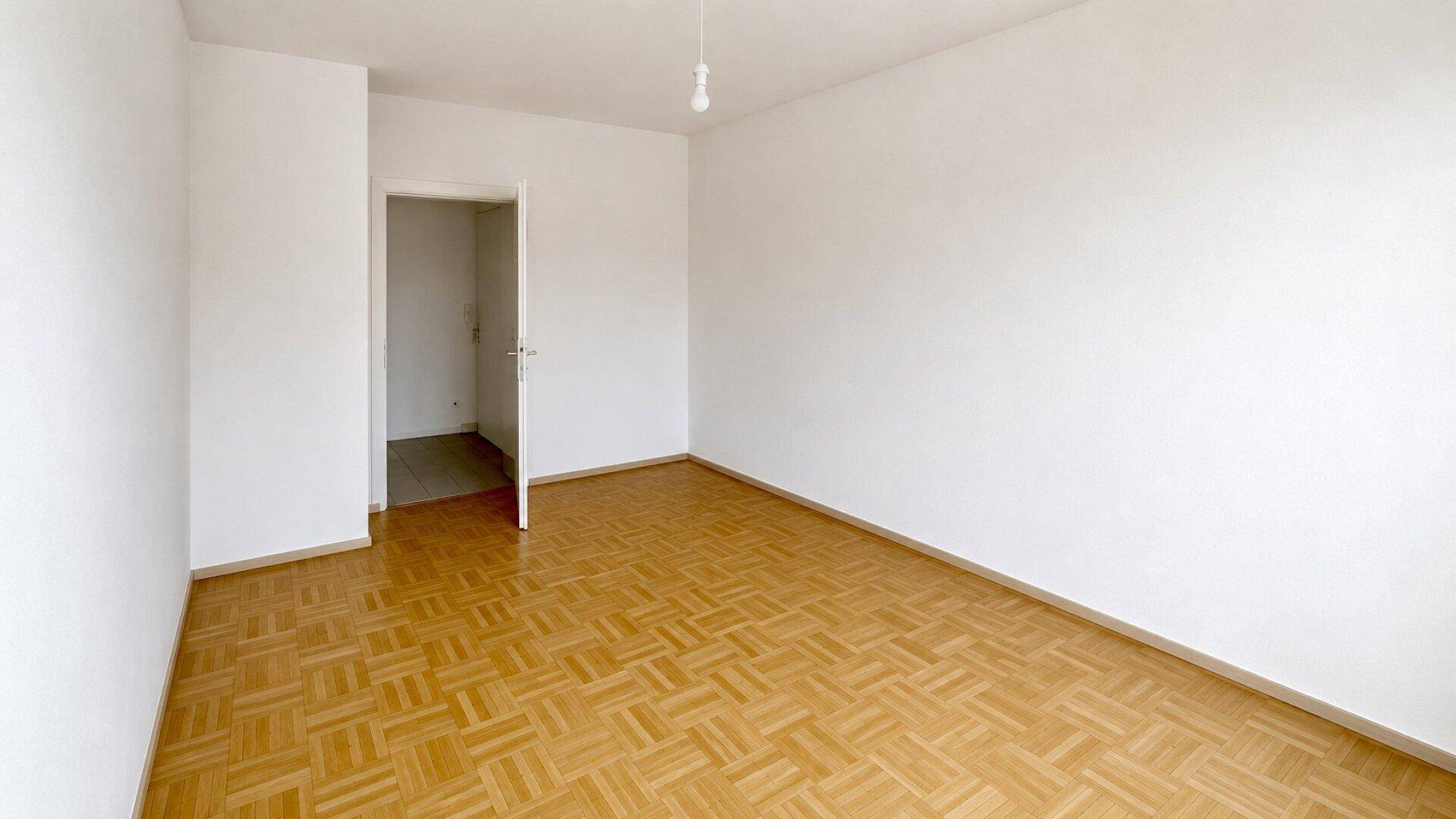 Geräumiges Zimmer mit hellem Parkettboden und Zugang zu weiteren Räumen.