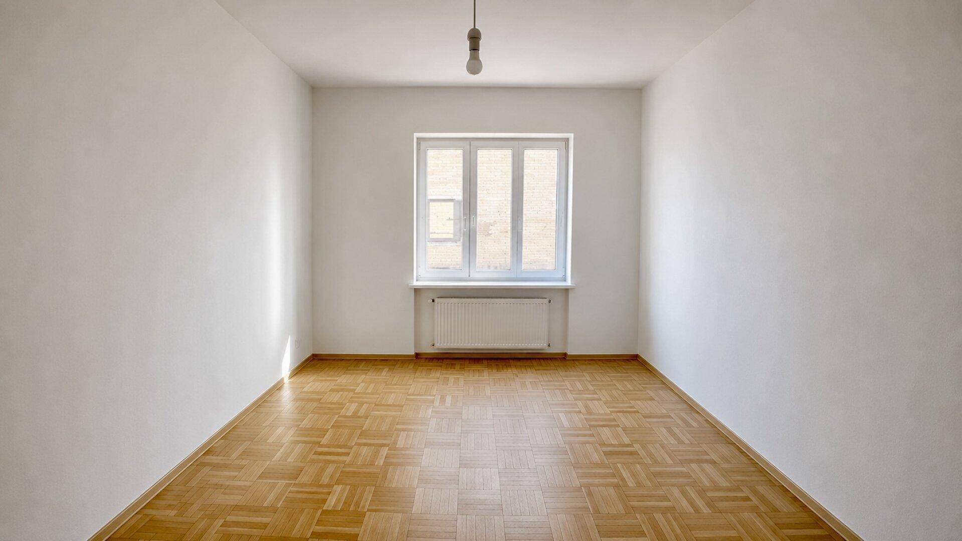 Lichtdurchflutetes Zimmer mit Holzparkett und einem großen Fenster, das viel Helligkeit spendet.