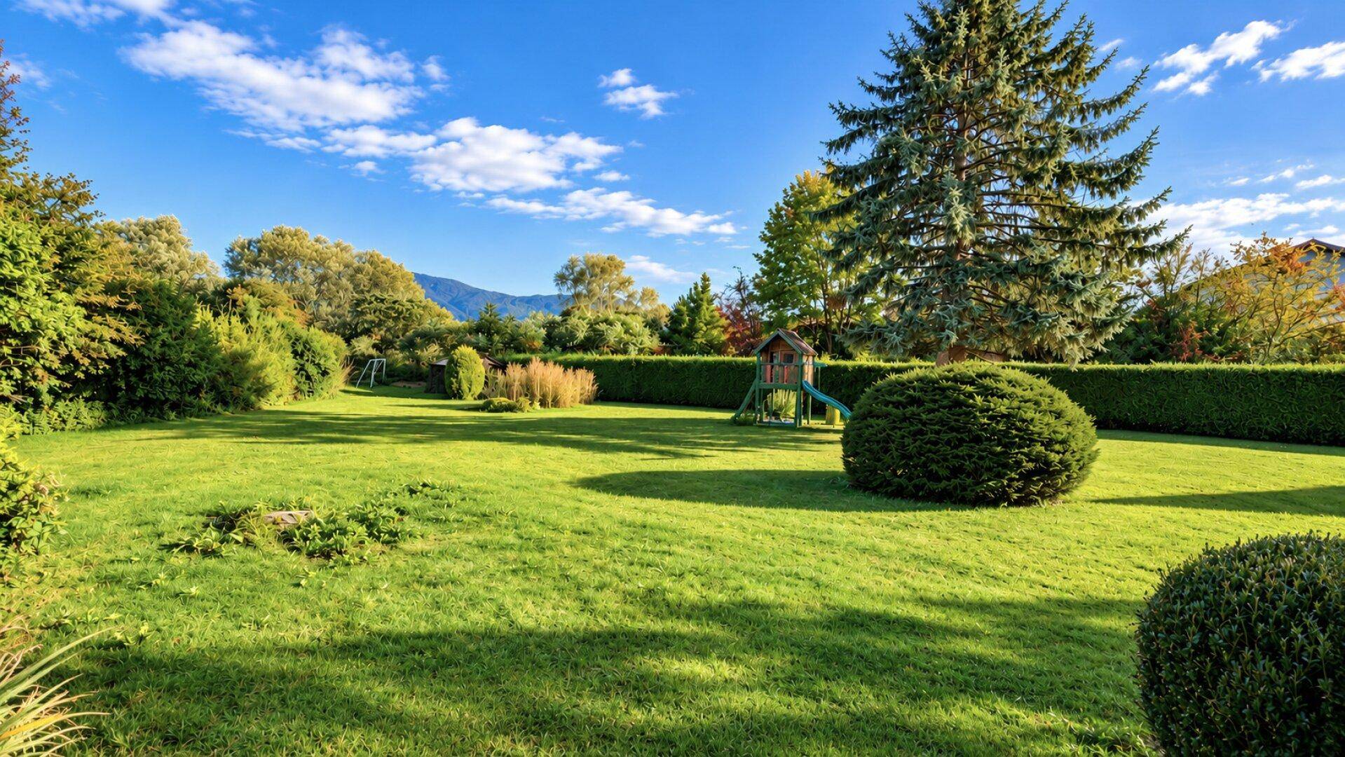 Weitläufiger Garten mit Spielplatz und gepflegter Hecke, umgeben von grüner Landschaft.
