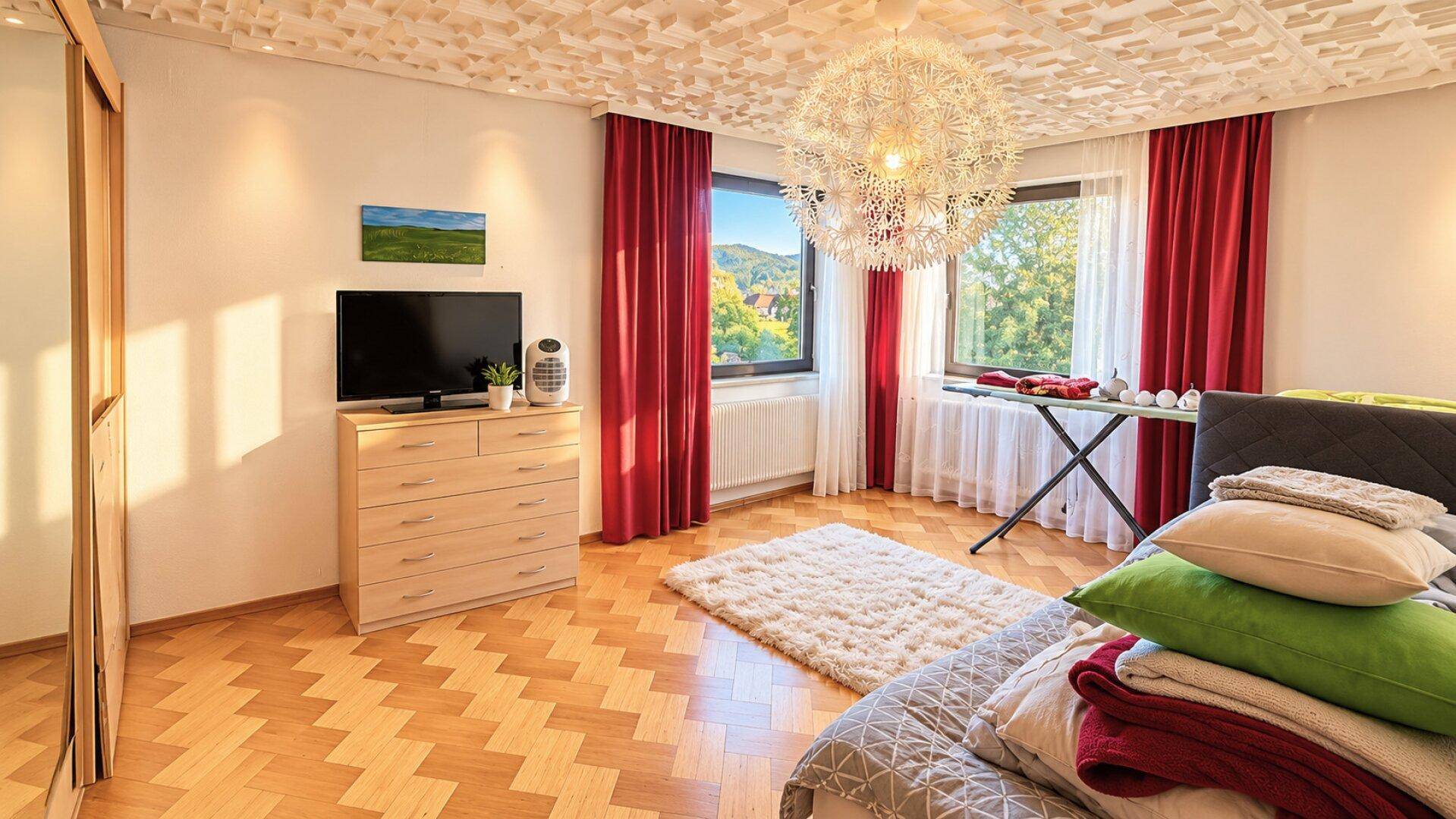 Helles Schlafzimmer mit Holzboden, großem Fenster und moderner Deckenleuchte.