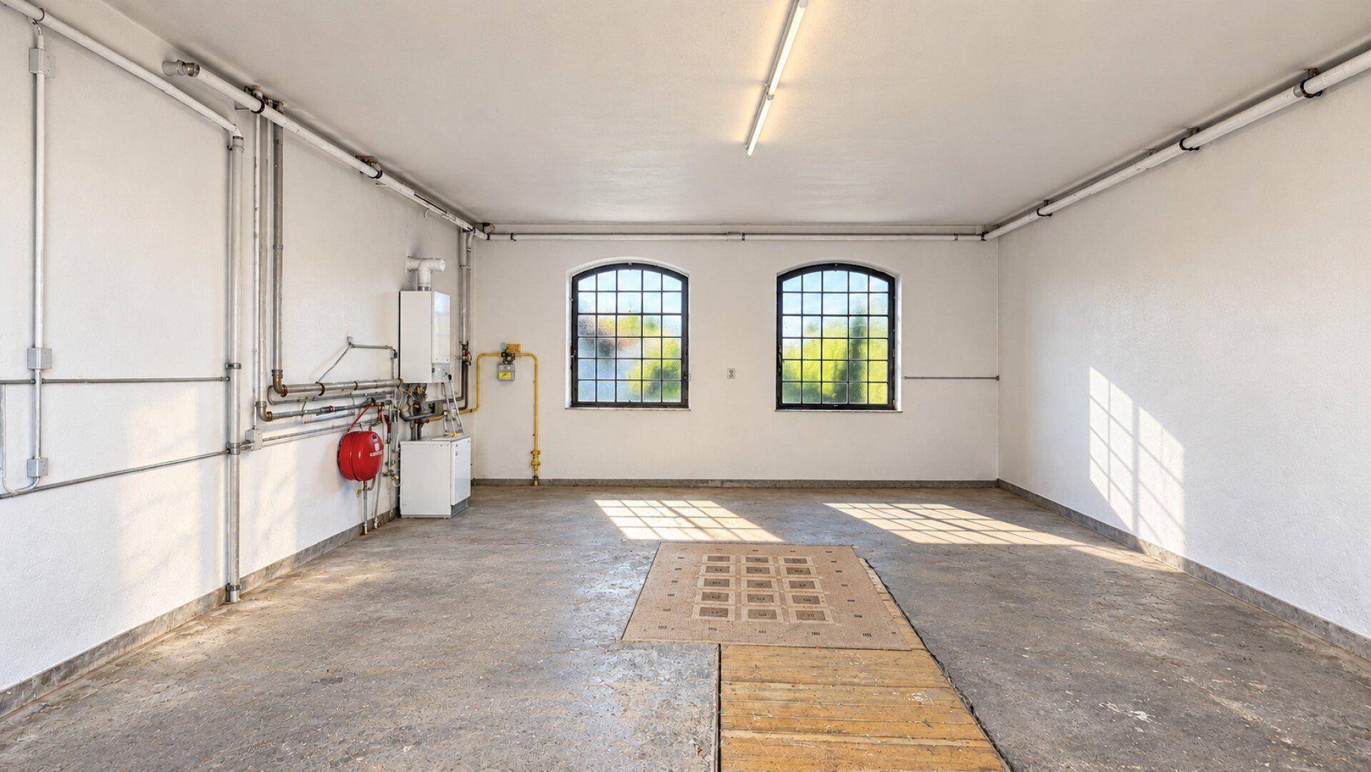 Geräumige Garage mit Betonboden, hohen Decken und zwei Fenstern.
