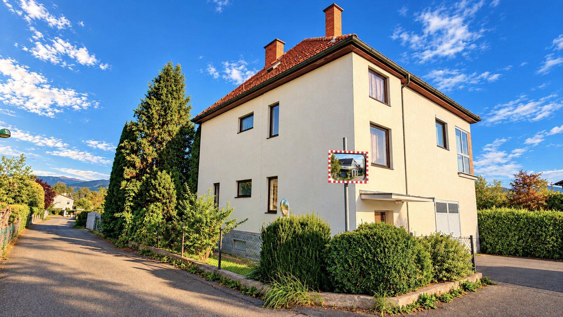 Seitenansicht eines Einfamilienhauses mit Zufahrtsstraße und einem Verkehrsspiegel.