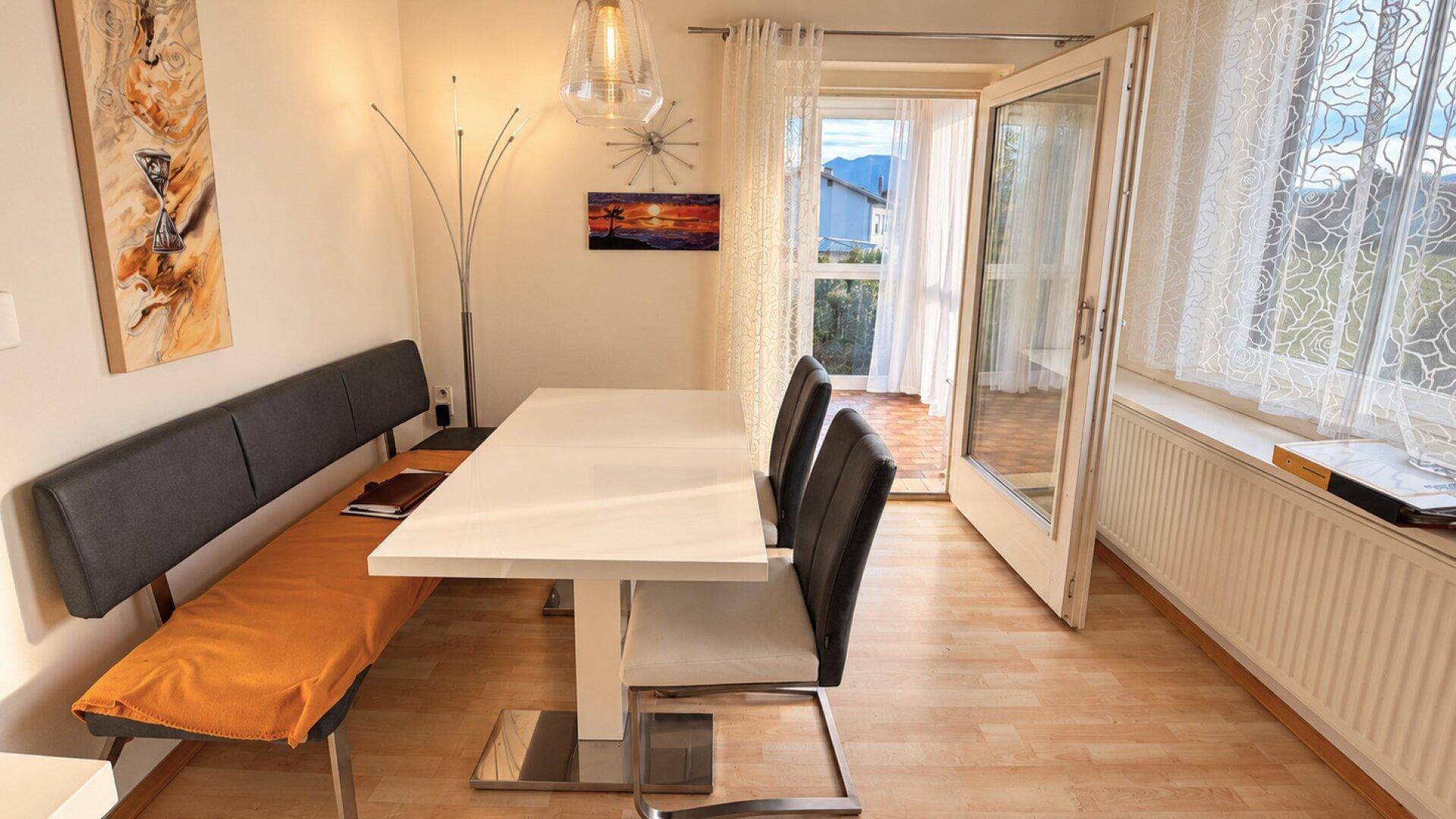 Essbereich mit modernem Esstisch, Sitzbank und Zugang zu einem Balkon oder einer Terrasse.