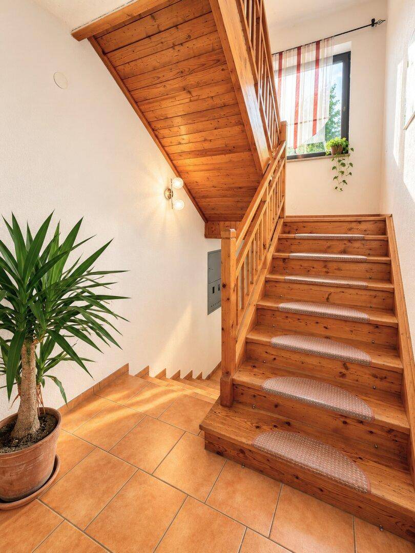 Holztreppe mit Fliesenboden im Eingangsbereich, beleuchtet durch ein Fenster.