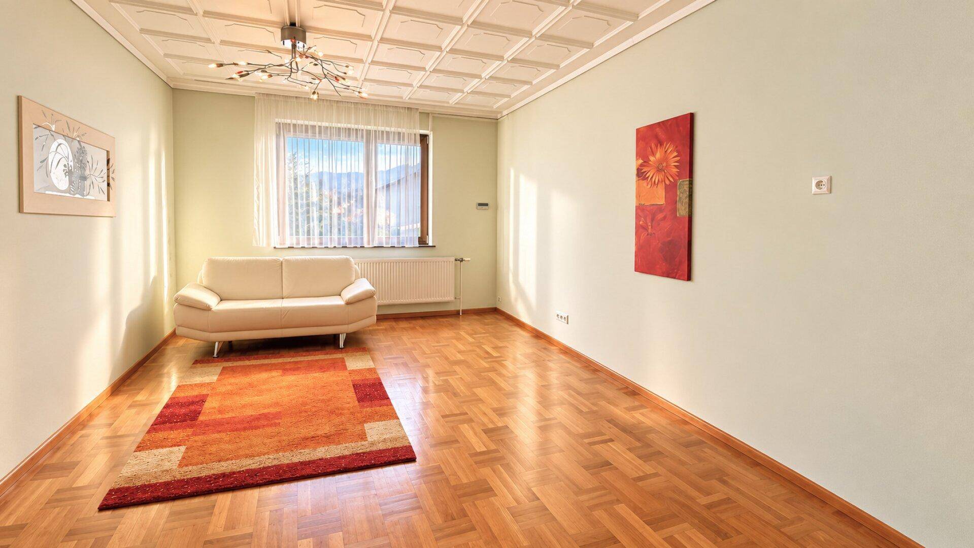 Geräumiges Wohnzimmer mit Fischgrätparkett, heller Couch und dekorativer Deckenverkleidung.