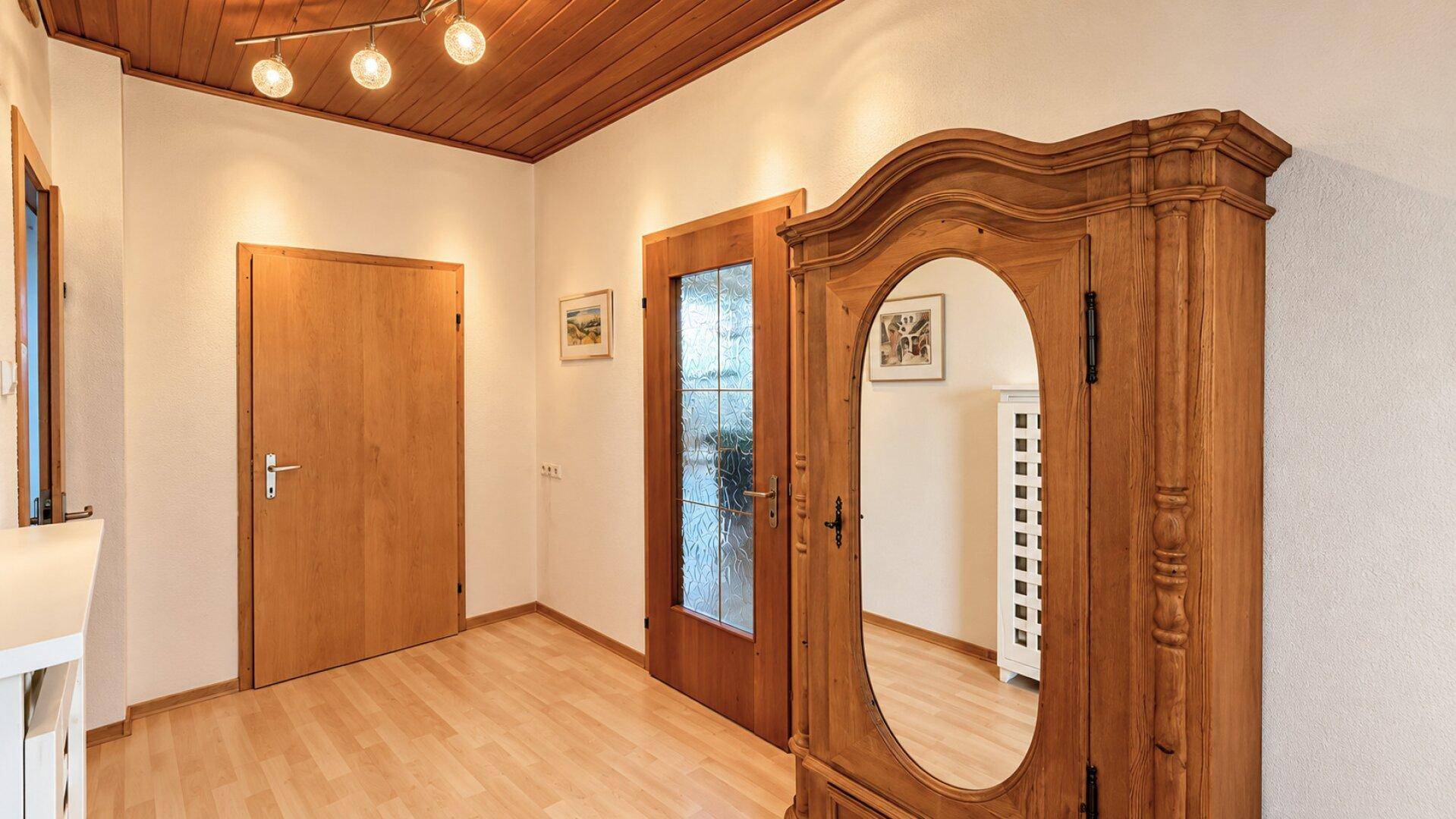 Heller Flur mit Holzdecke, Laminatboden und einem antiken Holzschrank mit Spiegel.