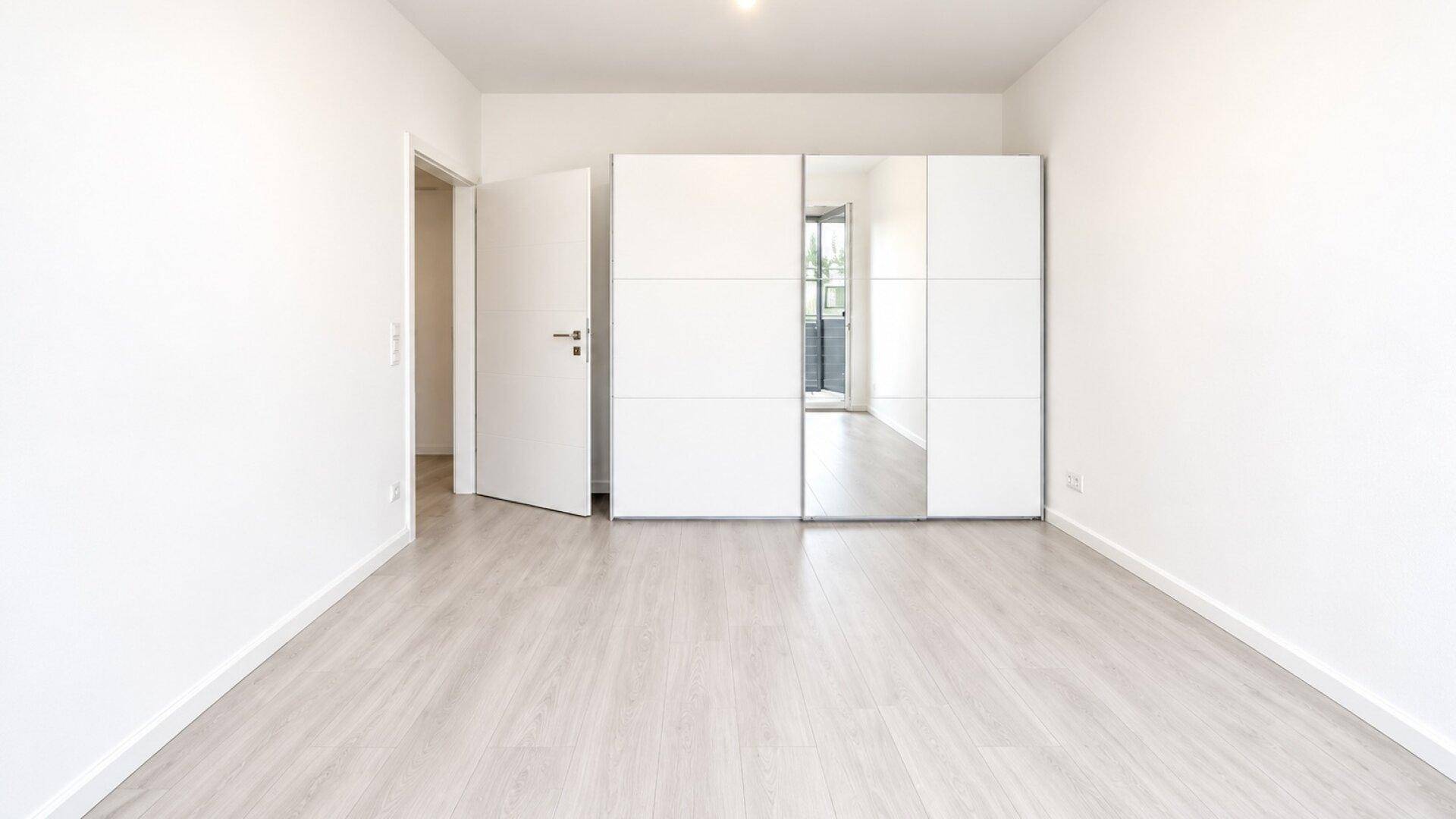 Helles Schlafzimmer mit modernem Laminatboden und einem großen Spiegelschrank.
