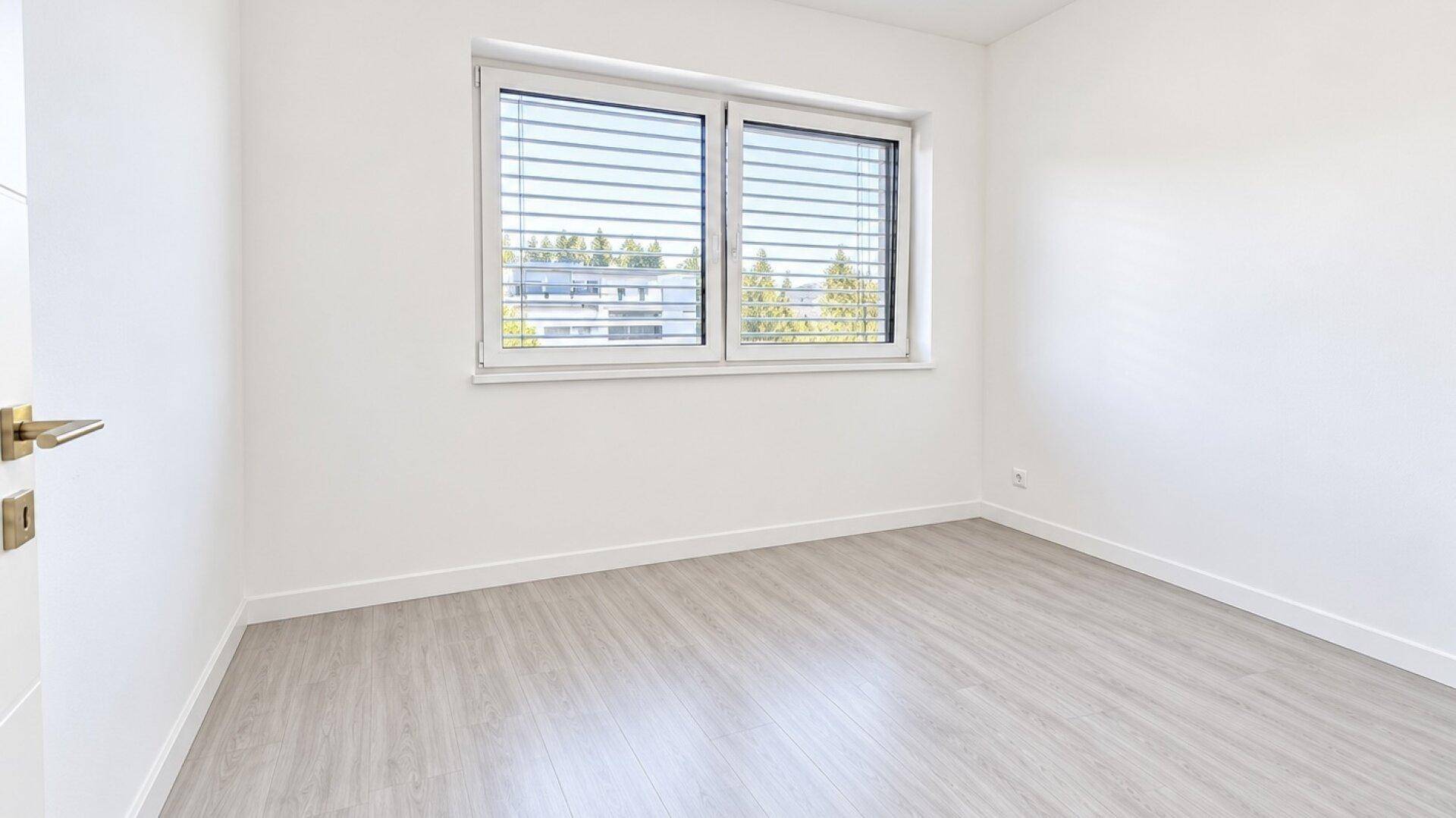 Heller Raum mit Laminatboden und Fenster mit Jalousien, ideal als Schlaf- oder Arbeitszimmer.
