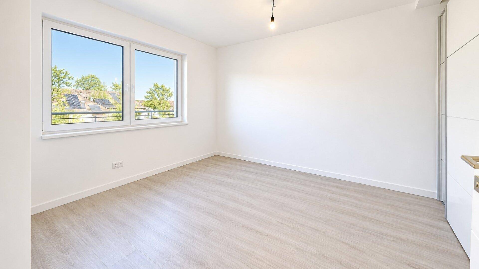 Geräumiges Schlafzimmer mit hellem Laminatboden und einem großen Fenster für viel Tageslicht.