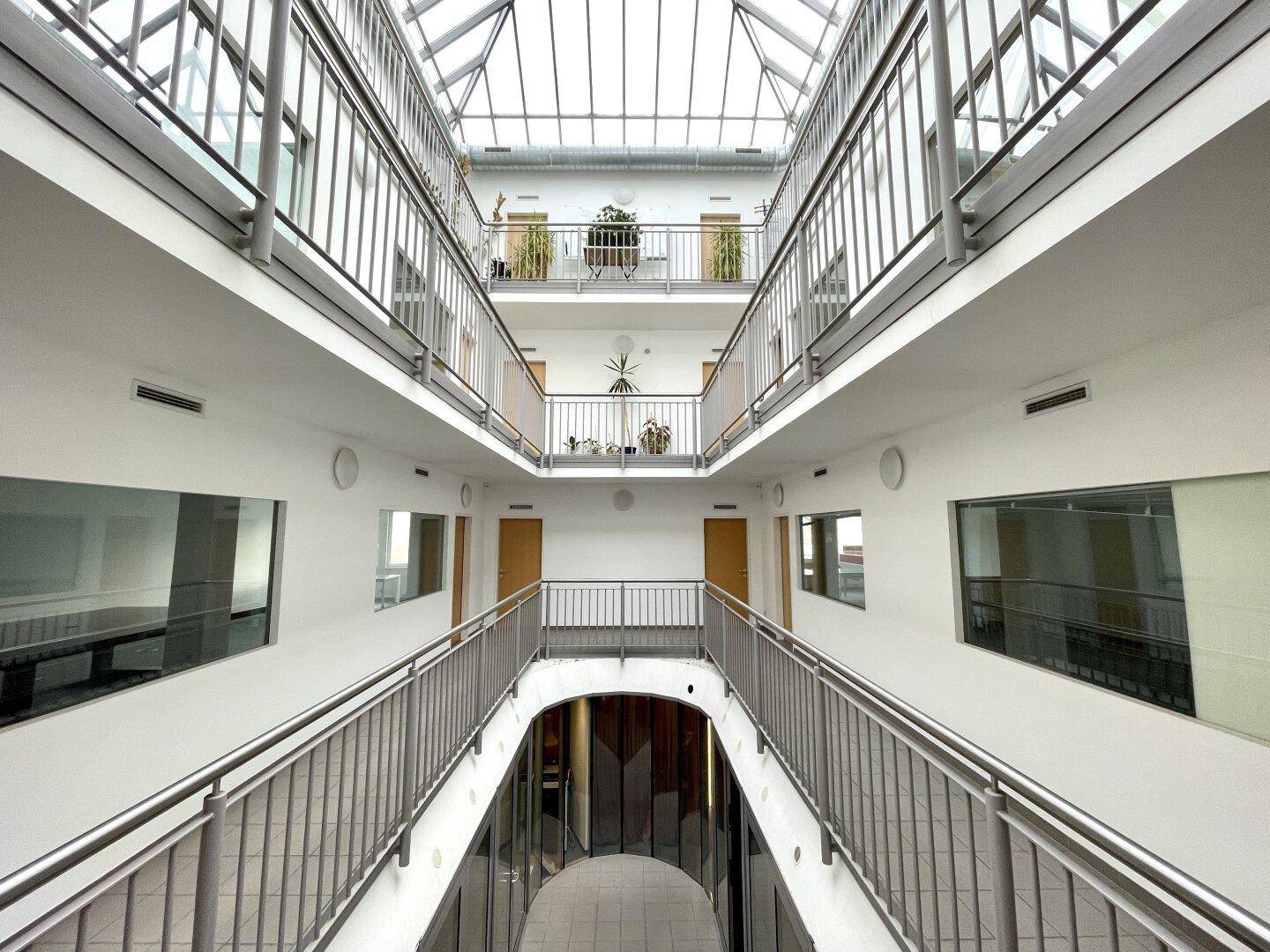 Heller, mehrstöckiger Innenhof mit Glasdach und umlaufenden Galerien, die zu den Büros führen.