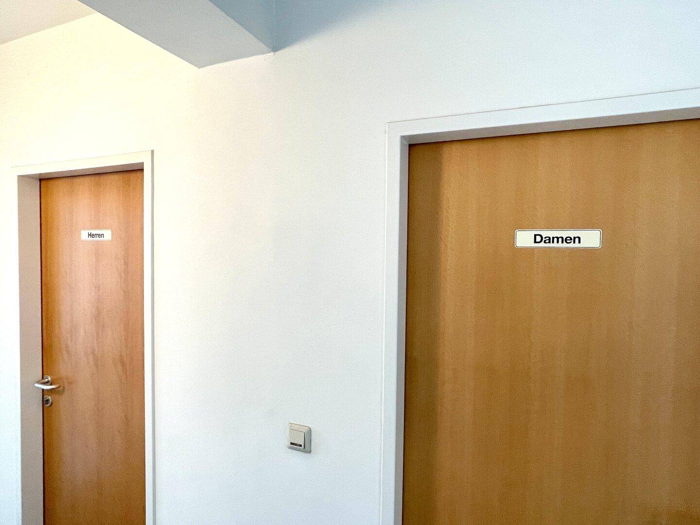 Schlichter Flur mit Türen zu den getrennten Damen- und Herren-Toilettenbereichen in einem Bürogebäude.
