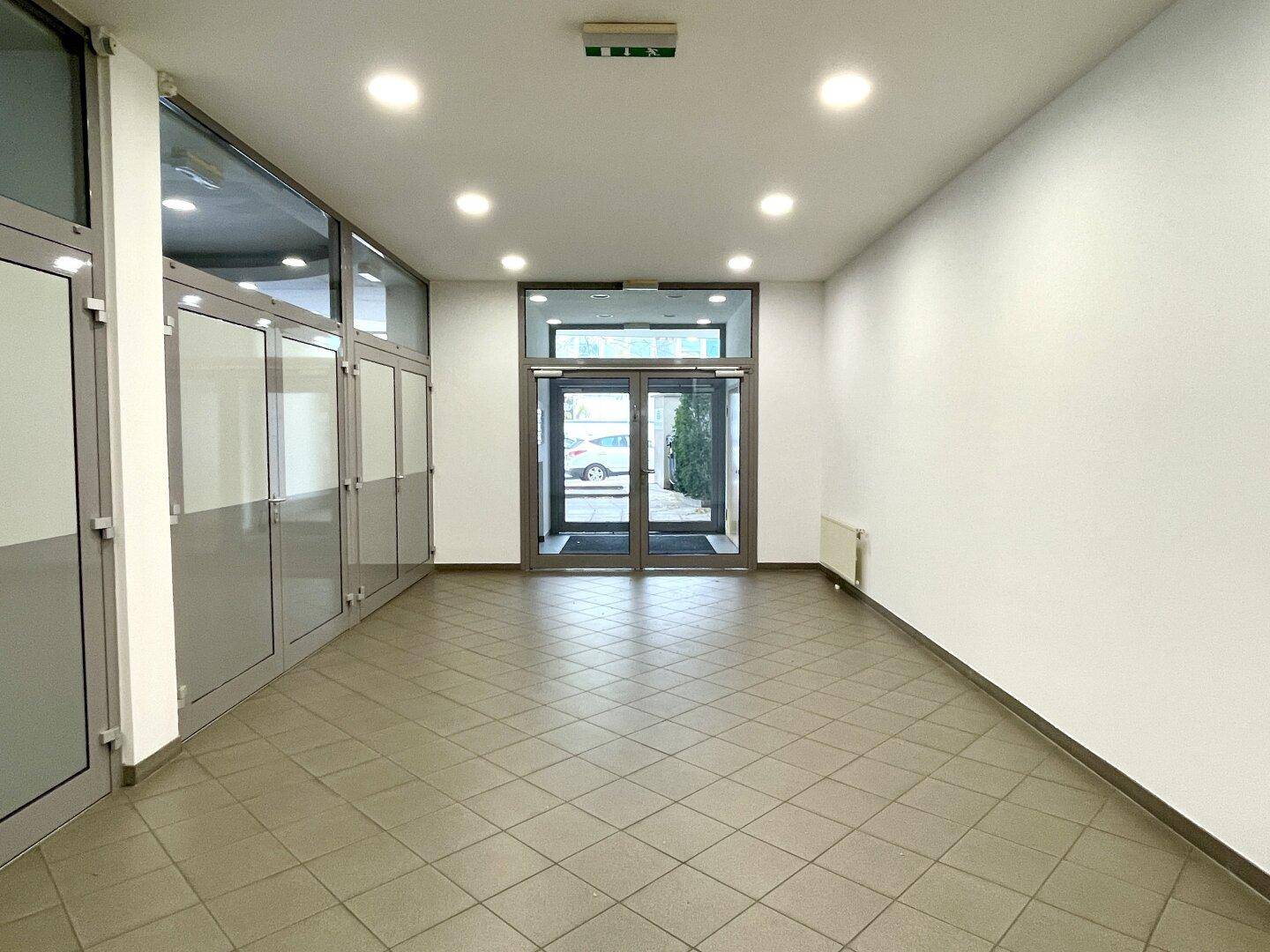 Geräumiger Eingangsbereich mit Fliesenboden und großen Glastüren, die viel Tageslicht hereinlassen.