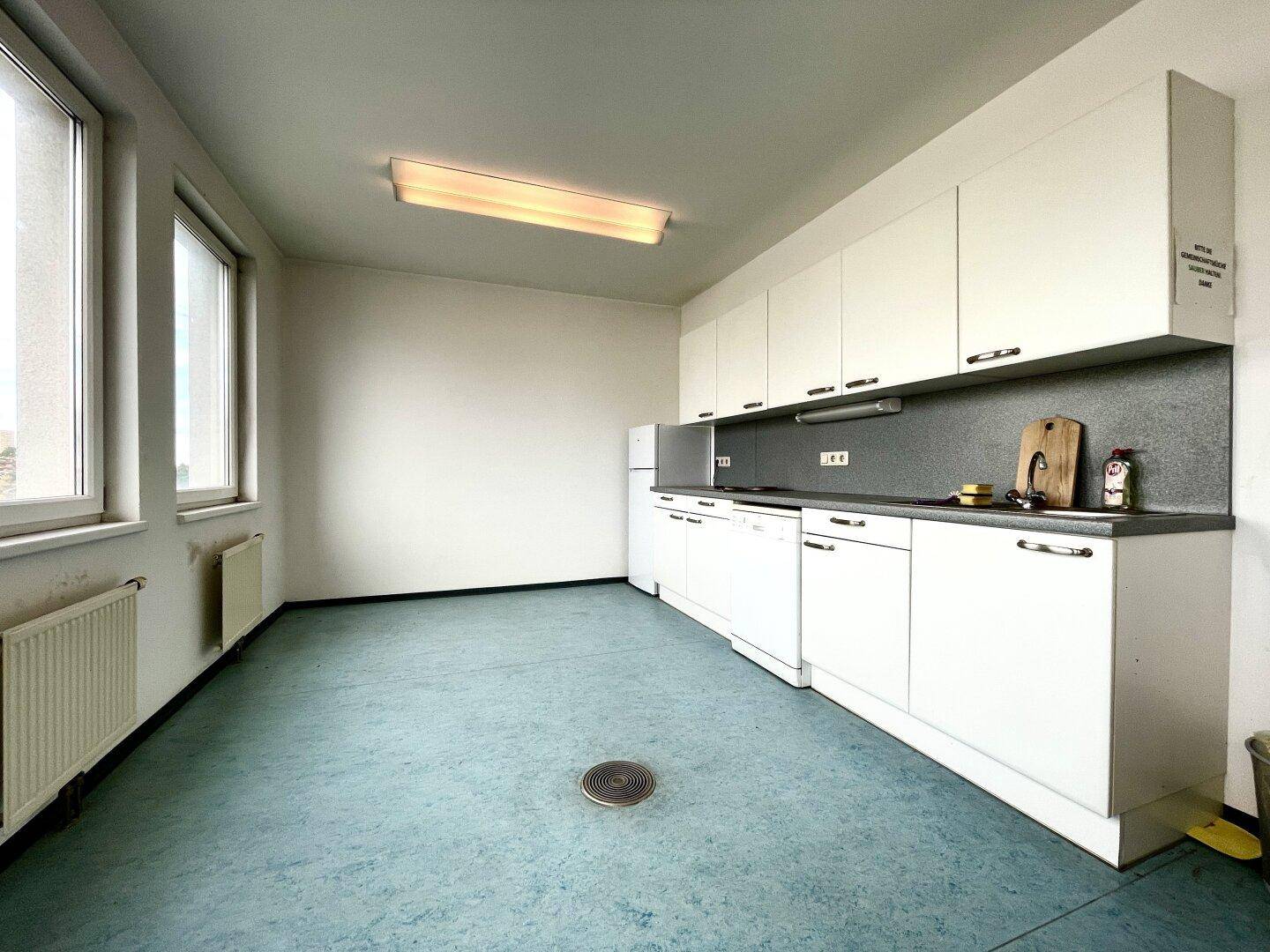 Funktionale Küche mit weißen Schränken, Spülmaschine und blauem Linoleumboden, ideal für Büronutzung.