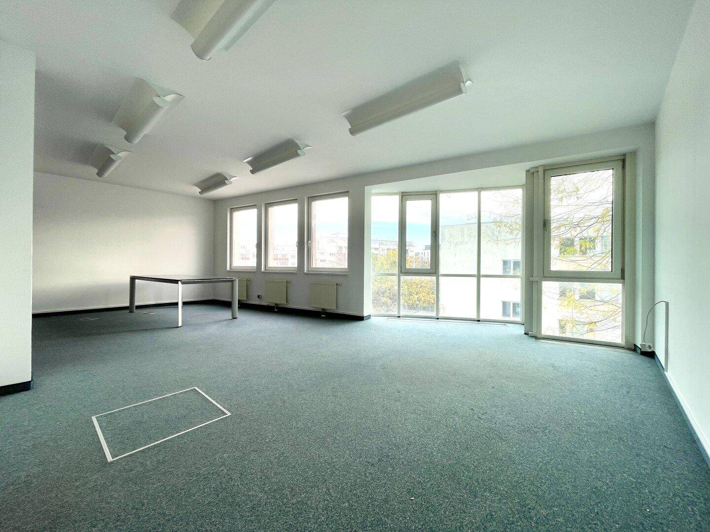 Großes, lichtdurchflutetes Büro mit Teppichboden und einer Fensterfront, die viel Tageslicht bietet.