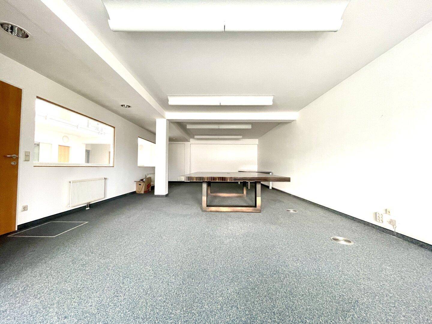 Helles Büro mit Teppichboden und einem großen Konferenztisch, ideal für Besprechungen.