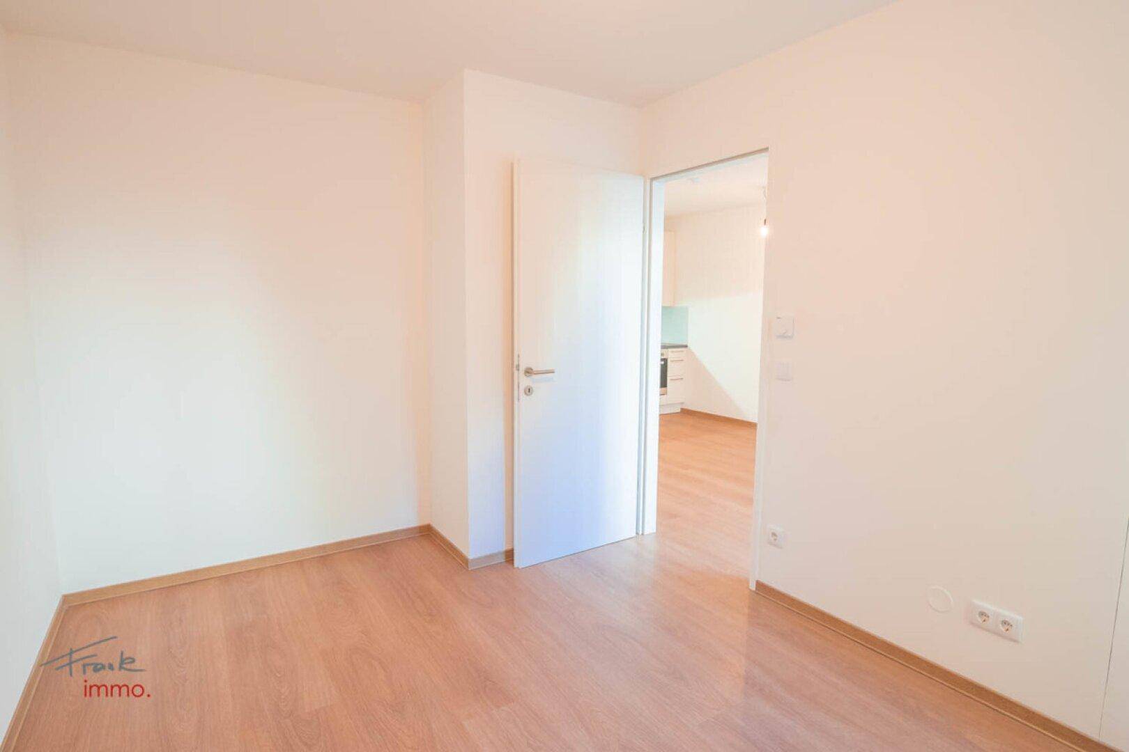 Heller, leerer Raum mit Holzboden und offener Tür zu einem weiteren Zimmer.