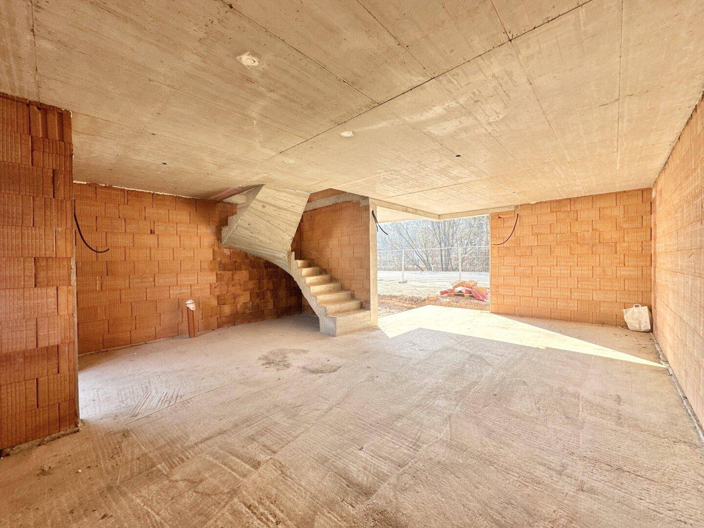 Heller Rohbau-Innenraum mit geschwungener Betontreppe und Blick nach draußen, ideal für offene Gestaltung.