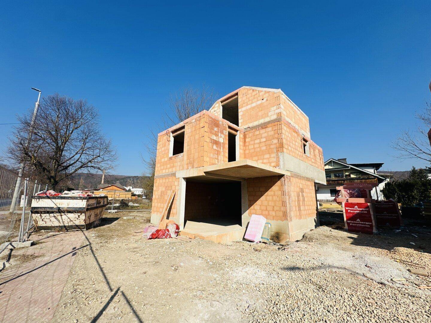 Rohbau eines Einfamilienhauses aus Ziegeln auf einer Baustelle mit weitem Blick.