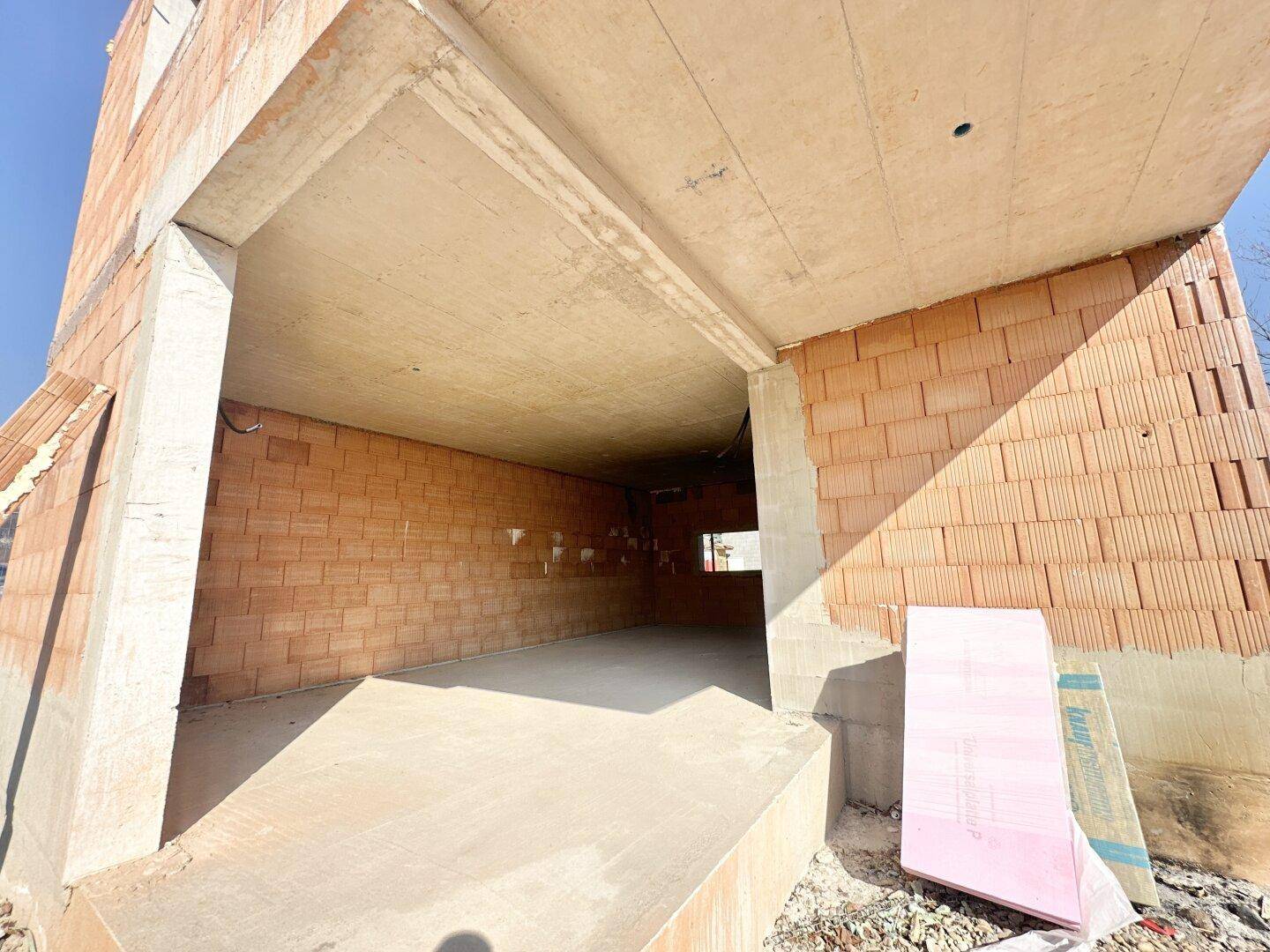 Unfertiger Garagenbereich im Erdgeschoss mit Betonboden und Ziegelwänden.
