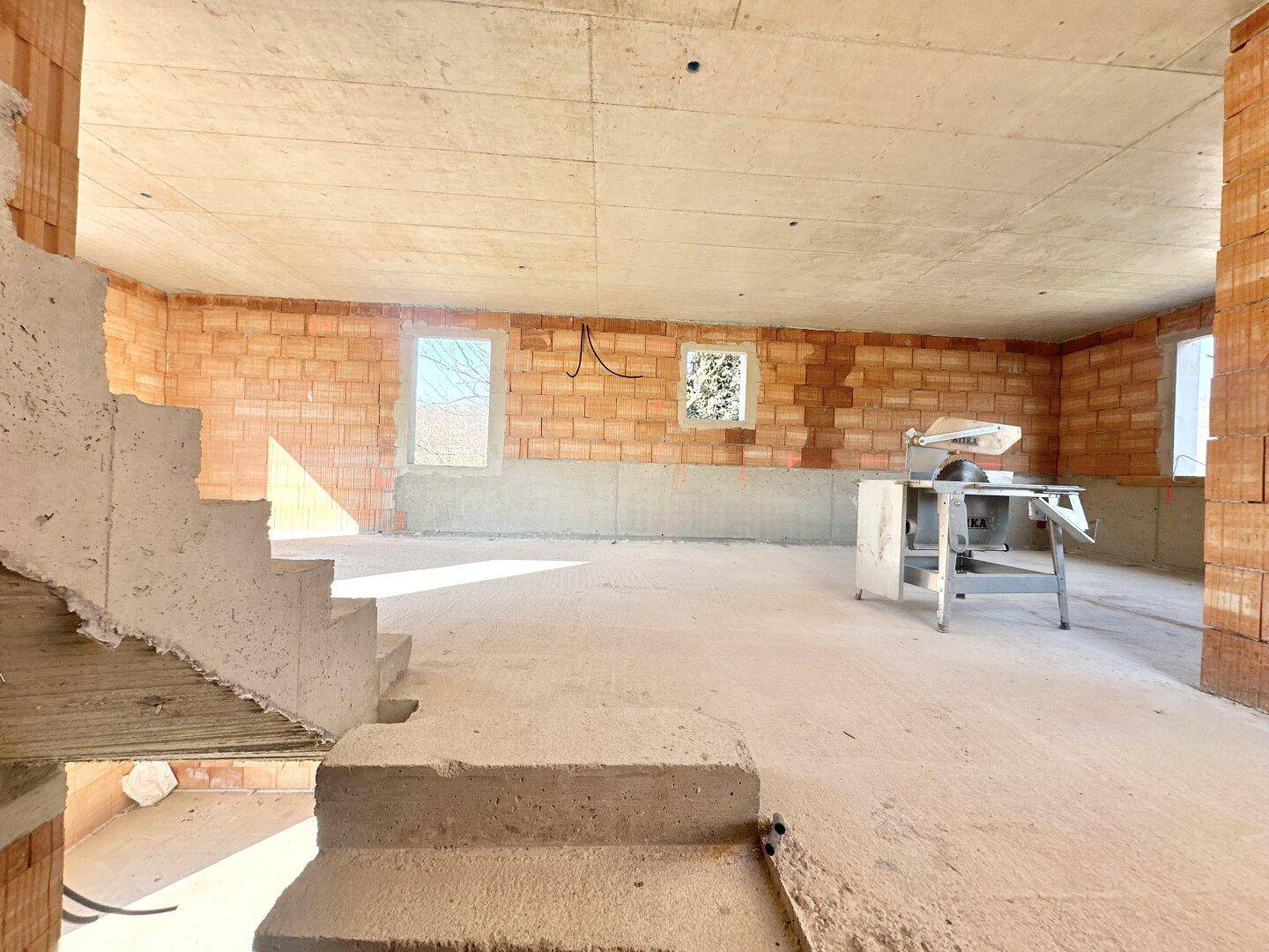 Rohbau-Raum mit Betonboden, Ziegelwänden und einem Baugerät, bereit für den Innenausbau des Hauses.