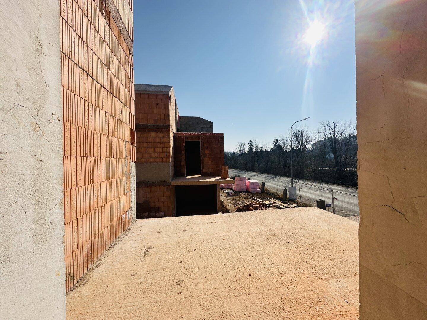 Blick von einer zukünftigen Terrasse auf die Umgebung und die angrenzende Straße unter strahlendem Himmel.
